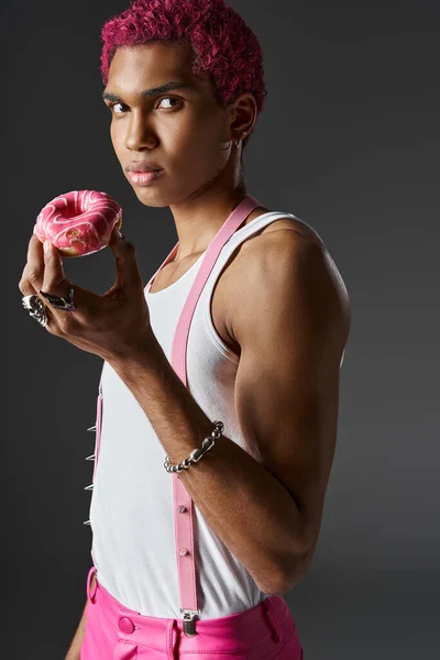 stock image stylish man in pink pants and suspenders with accessories posing with donut, fashion and style