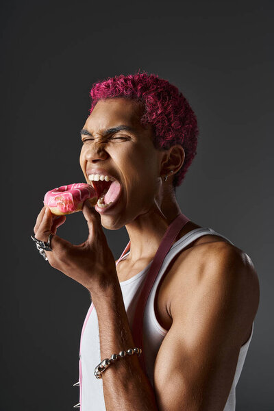 Воодушевленный красавец с розовыми волосами и аксессуарами, питающийся вкусным розовым пончиком, модой и стилем