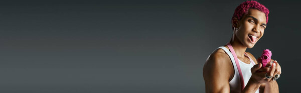 playful young african american man sticking out tongue and leveling his toy gun at camera, banner