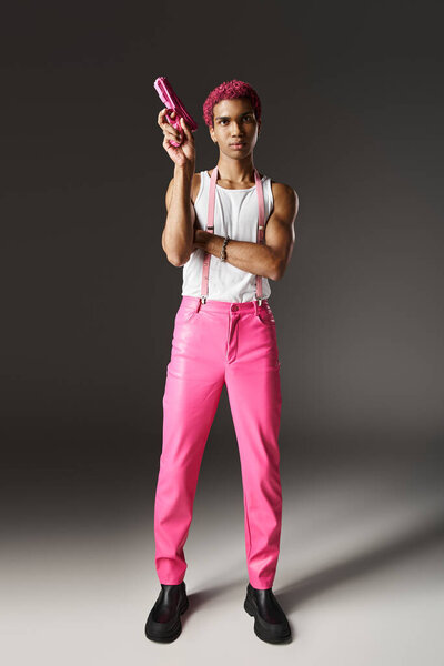 stylish african american man with pink hair pointing up his pink toy gun posing on gray backdrop