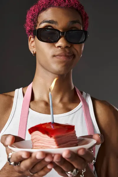 stock image good looking man posing with delicious cake with burning candle on gray background, fashion concept