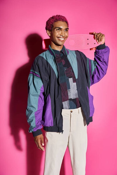 cheerful young male model posing unnaturally and smiling weirdly holding skateboard on shoulder