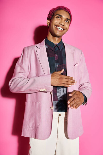 handsome young man acting unnaturally like doll smiling and posing on pink backdrop