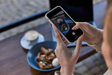 Bir kadının akıllı telefonuyla dondurma kepçesiyle Belçika waffle 'larının fotoğrafını çekerken görüntüsü.
