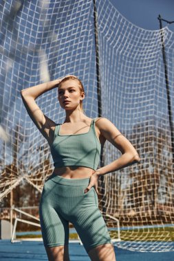 At kuyruklu genç bir kadın spor kıyafetleriyle, dışarıda çalışırken kalça hizasında poz veriyor.