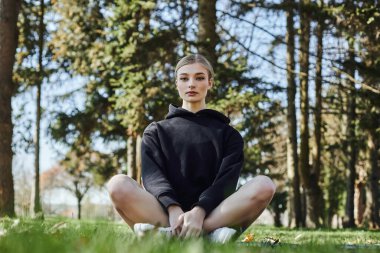 Parkta meditasyon yaparken mindere oturan sarışın ve formda bir kadın.