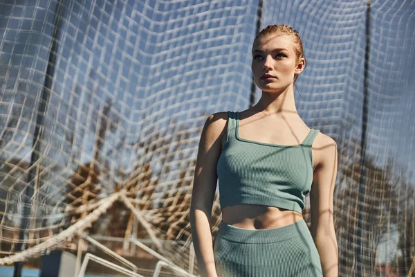 At kuyruklu güzel ve formda bir kadın açık havada çalışırken spor kıyafetinin yanında duruyor.