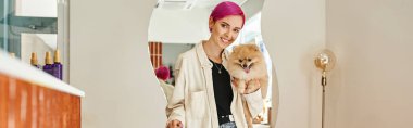Pomeranya soslu şık bir kadın köpek otelinde resepsiyon masasının yanındaki kameraya gülümsüyor.