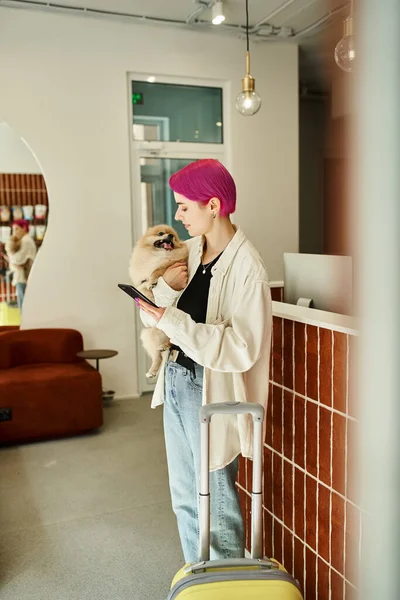 Stijlvolle Vrouw Met Pomeranian Spitz Smartphone Buurt Van Koffer Receptie — Stockfoto