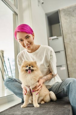 Mutlu ve şık köpek bakıcısı pomeranian spitz 'e sarılıyor ve evcil oteldeki kameraya bakıyor.