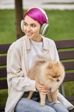 Pomeranya tükürüğüyle neşeli bir kadın kulaklıkla müzik dinliyor ve parka bakıyor.