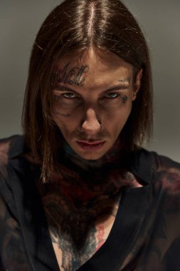 Yüzünde dövme olan genç bir adamın portresi doğrudan kameraya bakıyor, moda konsepti.