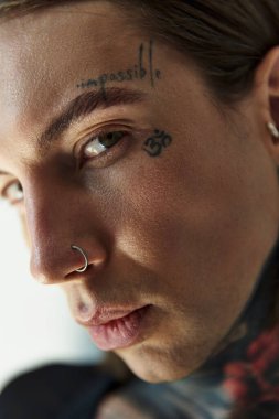 Yüzünde dövme ve piercing olan genç bir erkek modelin kamera görüntüsü, moda konsepti.