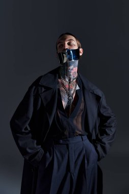 good looking man with tattoos in laced stylish mask posing on black backdrop, fashion concept clipart