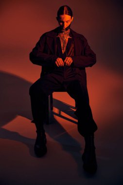 Sandalyeye oturmuş şık aksesuarlarıyla fütüristik maskeli seksi genç adam, moda konsepti.