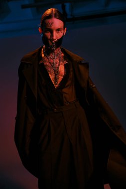 Dikey çekimde, bağcıklı fütürist maskeli yakışıklı genç adam kameraya bakıyor, moda konsepti