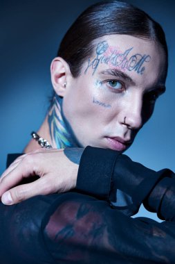 Çekici, dövmeli, şeffaf gömlekli ve piercingli genç bir adam. Kameraya, moda konseptine bakıyor.