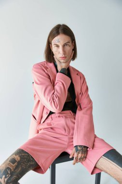 Genç erkek modelin el pençe divan oturduğu ve kameraya, modaya baktığı dikey bir çekim.