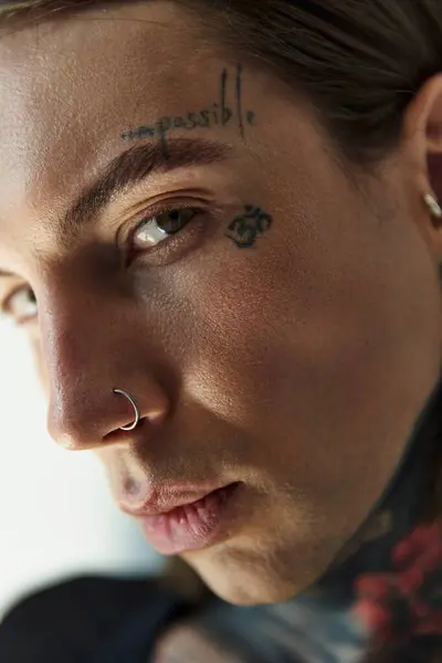 close up of young male model with tattoos on face and piercing looking at camera, fashion concept