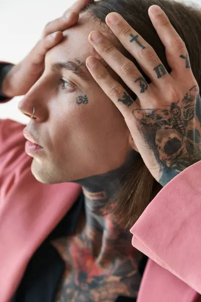 portrait of young fashionable man with tattoos on face and piercing with hands on face looking away
