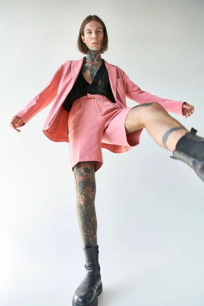 sexy young male model with tattoos in stylish vibrant attire with leg raised looking at camera