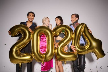 joyful interracial friends holding balloons with 2024 numbers near falling confetti, New Year party clipart