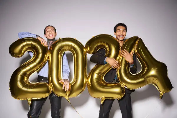 stock image happy interracial male friends holding balloons with 2024 numbers during party, New Year concept