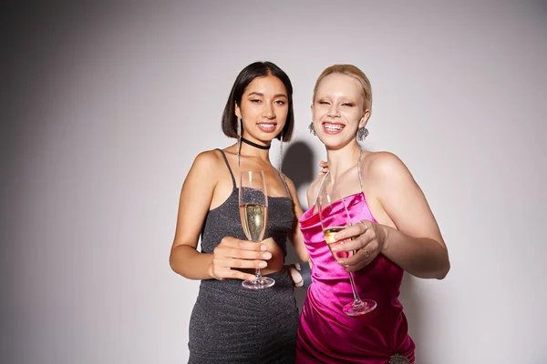 charming female friends in party dresses holding champagne glasses grey background, New Year