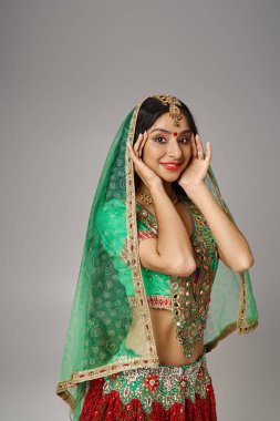 Bindi ve peçeli, ulusal giysiler içindeki çekici Hintli kadın kameraya bakıyor, elleri yüze yakın.