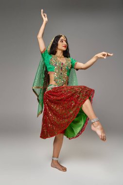 Gri arka planda dans ederken bindi noktasıyla işaret eden yeşil choli giymiş güzel Hintli kadın.