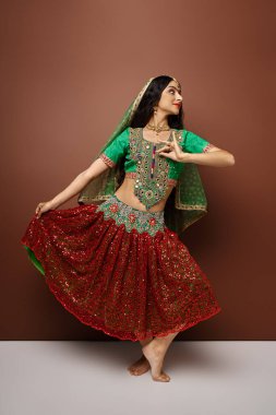 beautiful indian woman in traditional attire with veil and bindi dancing actively and looking away clipart