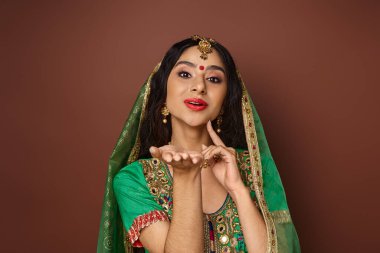 Bindi noktalı yeşil peçeli neşeli Hintli kadın. Elleri yüze yakın poz veriyor ve kameraya bakıyor.