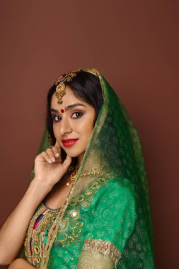 Bindi noktalı, yeşil peçeli, poz veren ve kameraya bakan güzel Hintli kadının dikey görüntüsü.
