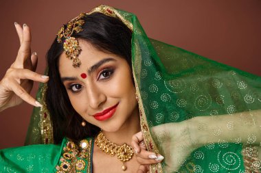 Bindi noktalı ve yeşil peçeli çekici Hintli kadın kameraya bakıyor.