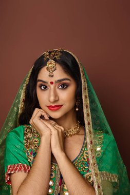 Yeşil peçeli ve alnında Bindi noktasıyla kameraya bakan güzel Hintli kadının dikey görüntüsü.