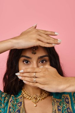 Ulusal kostümlü Hintli bir kadının elleriyle yüzünü örterken aktif dans ederken çekilmiş dikey bir fotoğrafı.