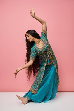 beautiful indian woman in traditional clothes gesturing while dancing actively on pink backdrop clipart