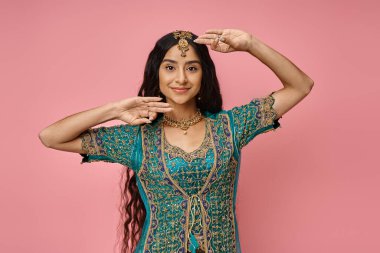 attractive young indian female model in national costume gesturing while dancing on pink background clipart