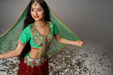 Ulusal kostümlü neşeli genç Hintli kadın konfetiye poz verip gözlerini kaçırıyor.