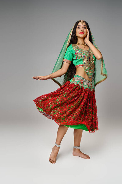 cheerful good looking indian woman posing in motion dressed in national costume, gray backdrop
