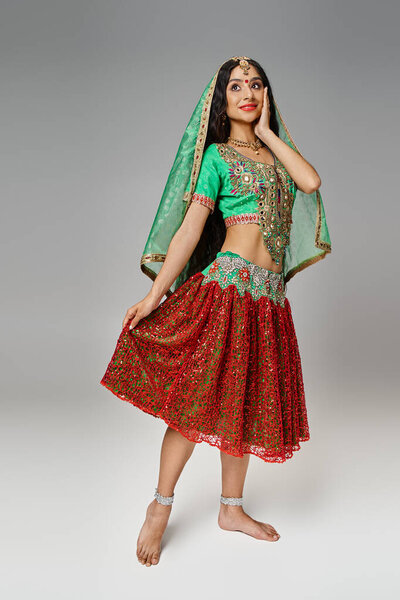 vertical shot of attractive dreamy indian woman with bindi dot posing in motion on gray backdrop