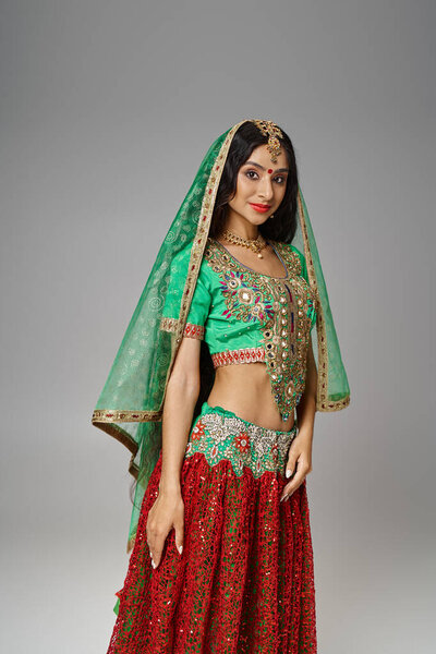 vertical shot of joyous indian woman in green choli and red skirt with bindi dot looking at camera