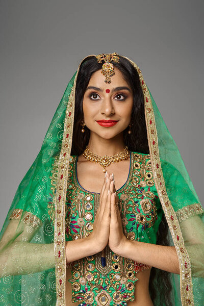 привлекательная индийская модель с точкой бинди на лбу и зеленой вуалью, молящаяся и смотрящая в сторону