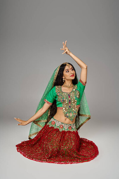 vertical shot of young indian woman in red skirt sitting on floor gesturing and looking away