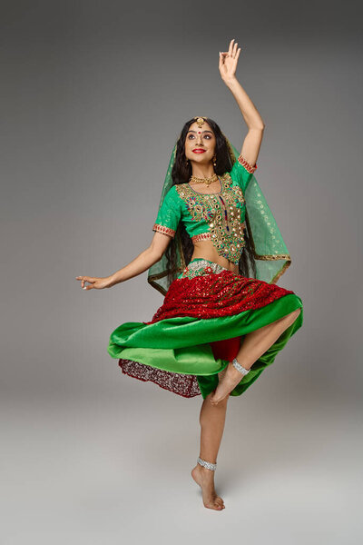 young indian woman in national attire standing on one leg with arm raised while dancing actively