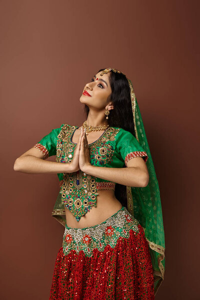 vertical shot of indian woman with bindi and green veil showing praying gesture and looking away