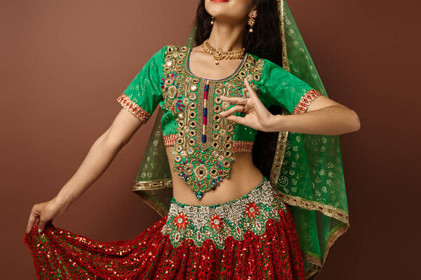 focus on hands of young indian woman in national attire gesturing while dancing on brown backdrop