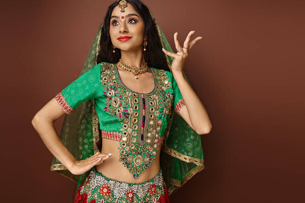 attractive indian female model in green choli with bindi dot gesturing while dancing, looking away