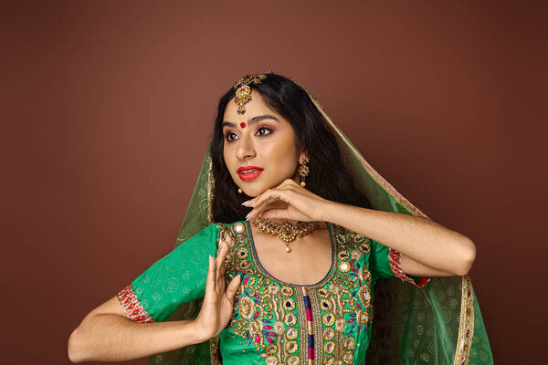 beautiful young indian woman in traditional costume with accessories gesturing and looking away