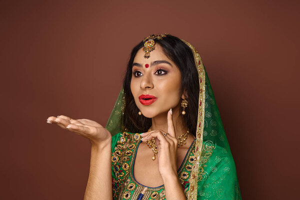 привлекательная молодая индийская женщина в зеленой вуали и бинди точка жестом активно и глядя в сторону